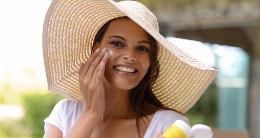 woman applying sunscreen with hat on 