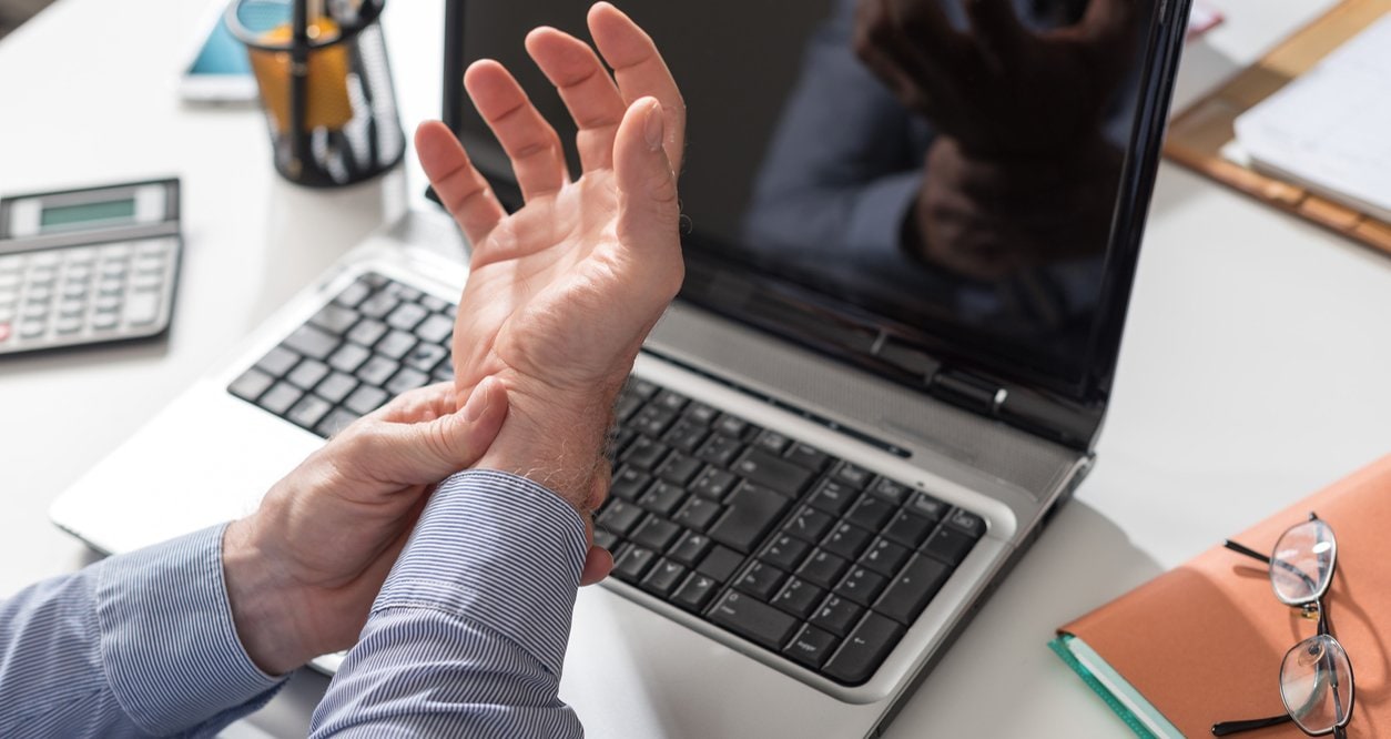 man grasping wrist over his laptop