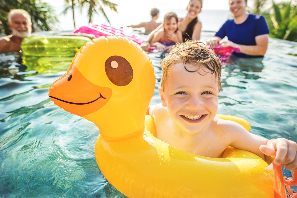 little boy in pool float smiling with family behind him