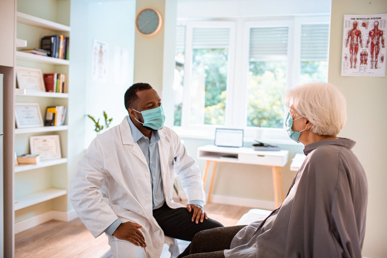 masked doctor speaking with patient